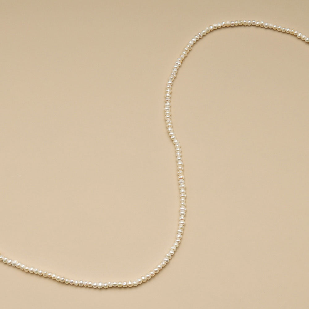 A string of 2mm seed pearls on brown cloth.