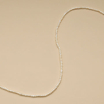 A string of 2mm seed pearls on brown cloth.