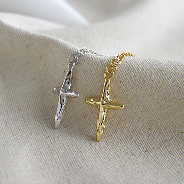 Gold cross pendant and silver cross pendant on a rutic cloth side by side.