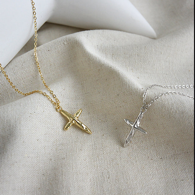 Gold cross pendant and silver cross pendant on a rutic cloth.