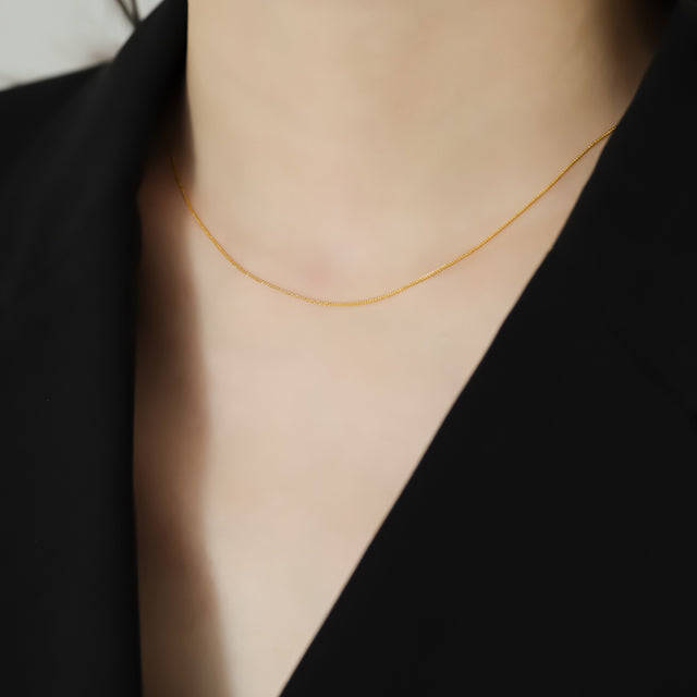 Women in black wear 18k thin gold chain.