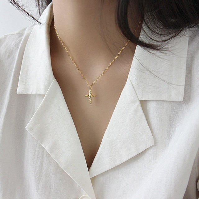 Gold cross pendant necklace on women's neck.