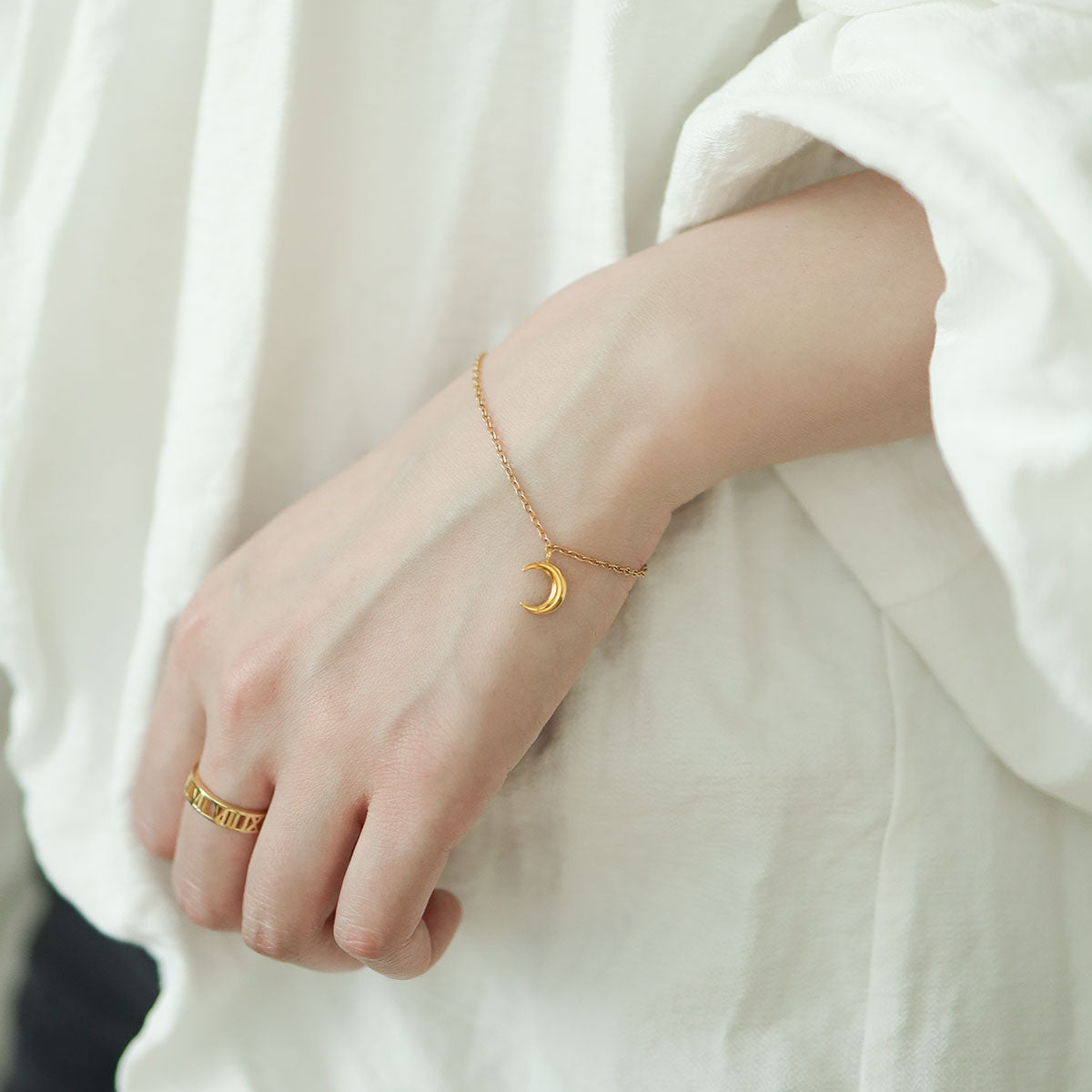 Women wear lunar gold bracelet and gold band ring.