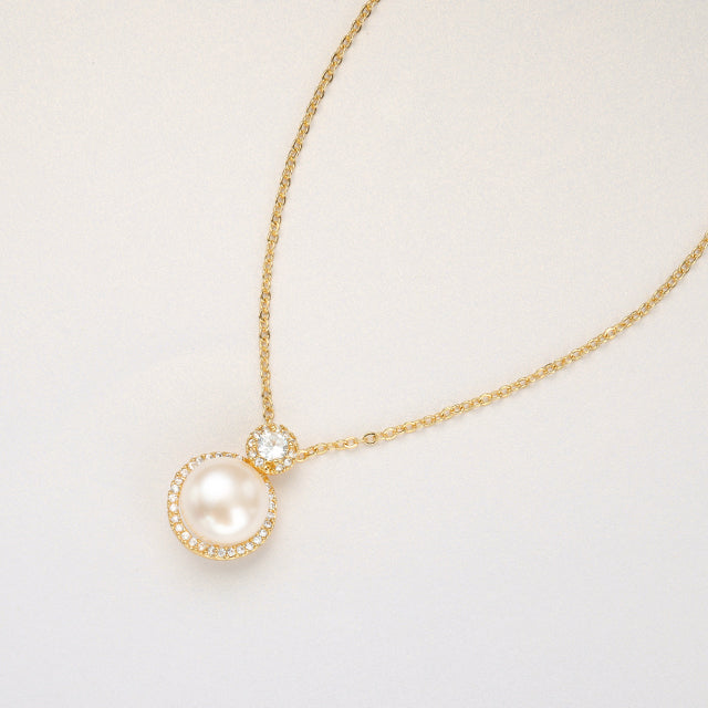 A natural pearl pendant necklace on cream paper.