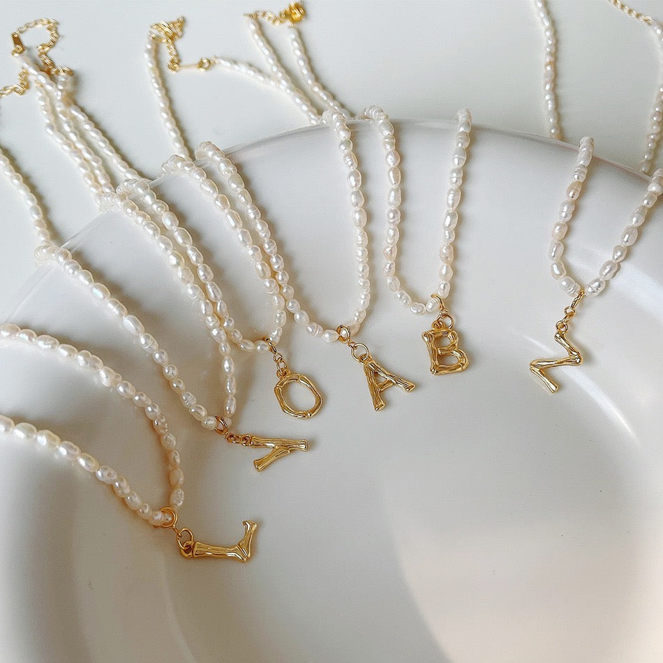 Pearl necklace with initial charm on white plate.