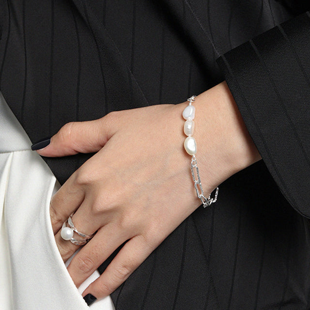 A woman dress in black wear silver pearl bracelet and silver pearl ring.