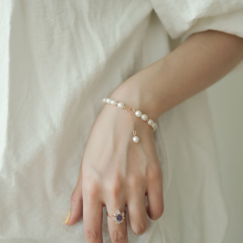 Women in white wear a simple pearl bracelet and a diamond ring.